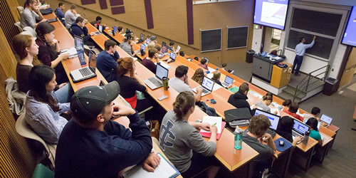 A lecture hall filled with individuals attentively sitting in front of laptops.