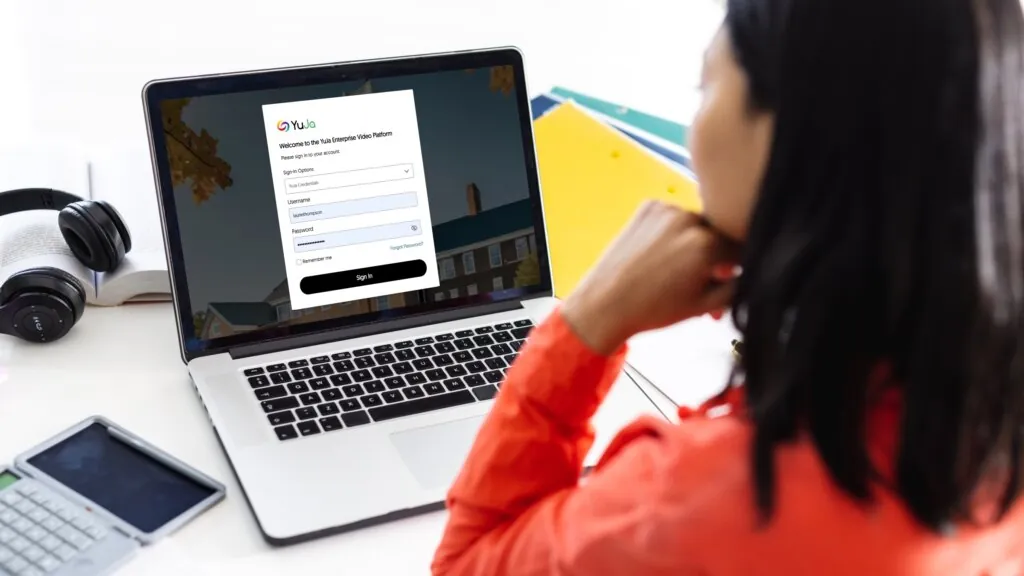 A woman is at her desk, signing into YuJa on her laptop.