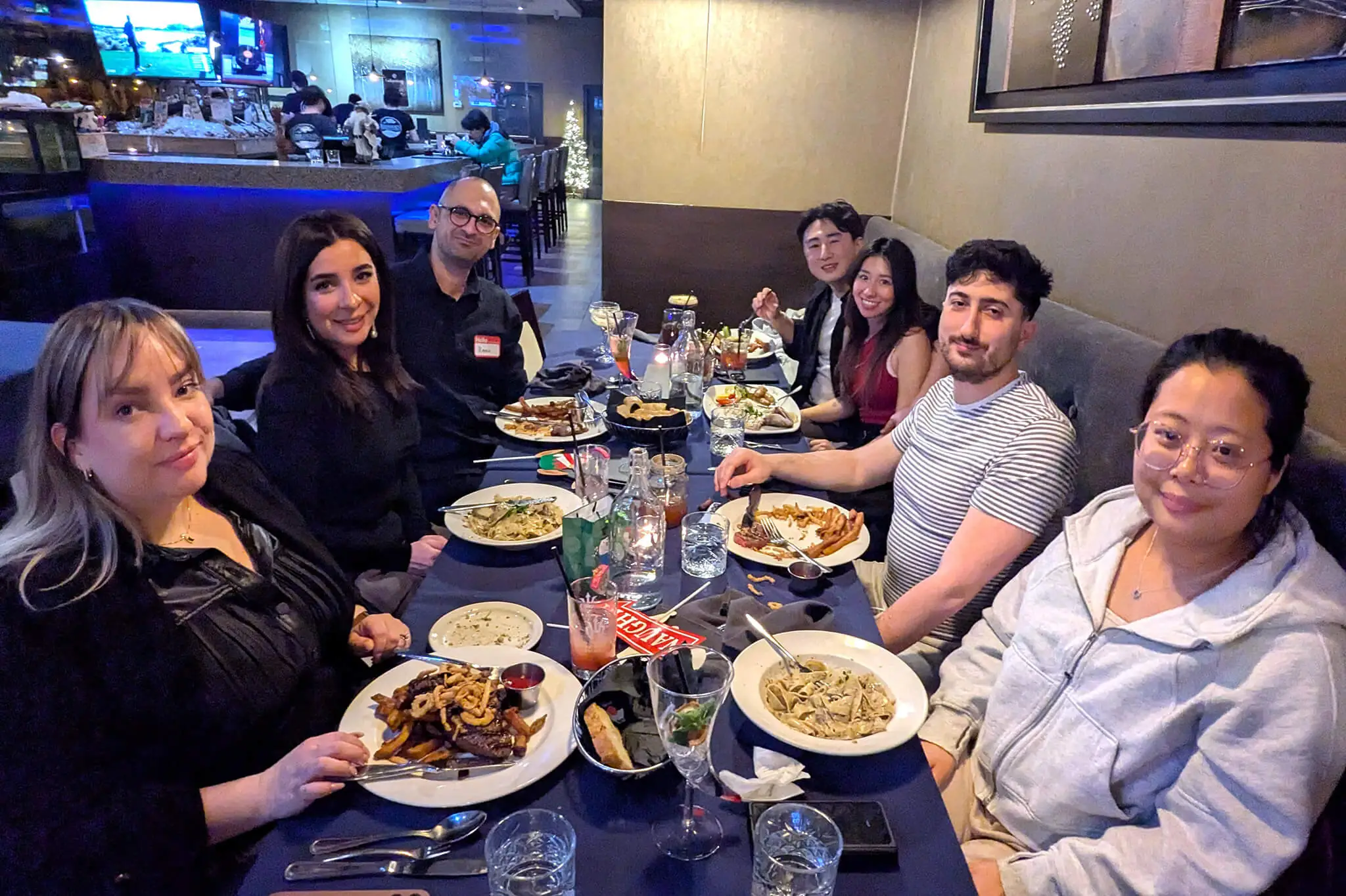 A group of YuJa team members gathered around a table enjoying a meal together, fostering camaraderie and collaboration.