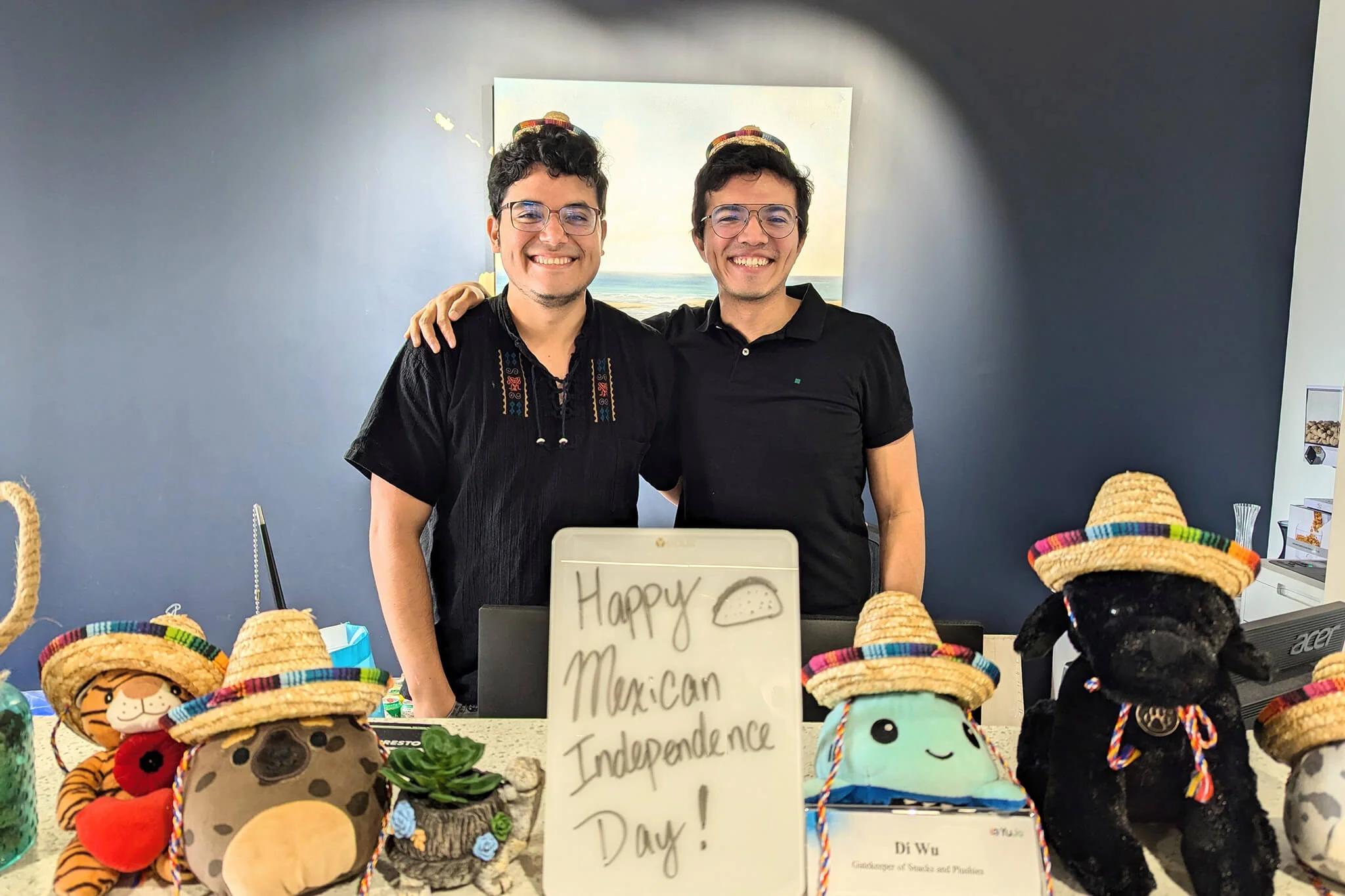 Two YuJa team members in black shirts and hats pose with a sign reading Happy Mexican Independece Day.