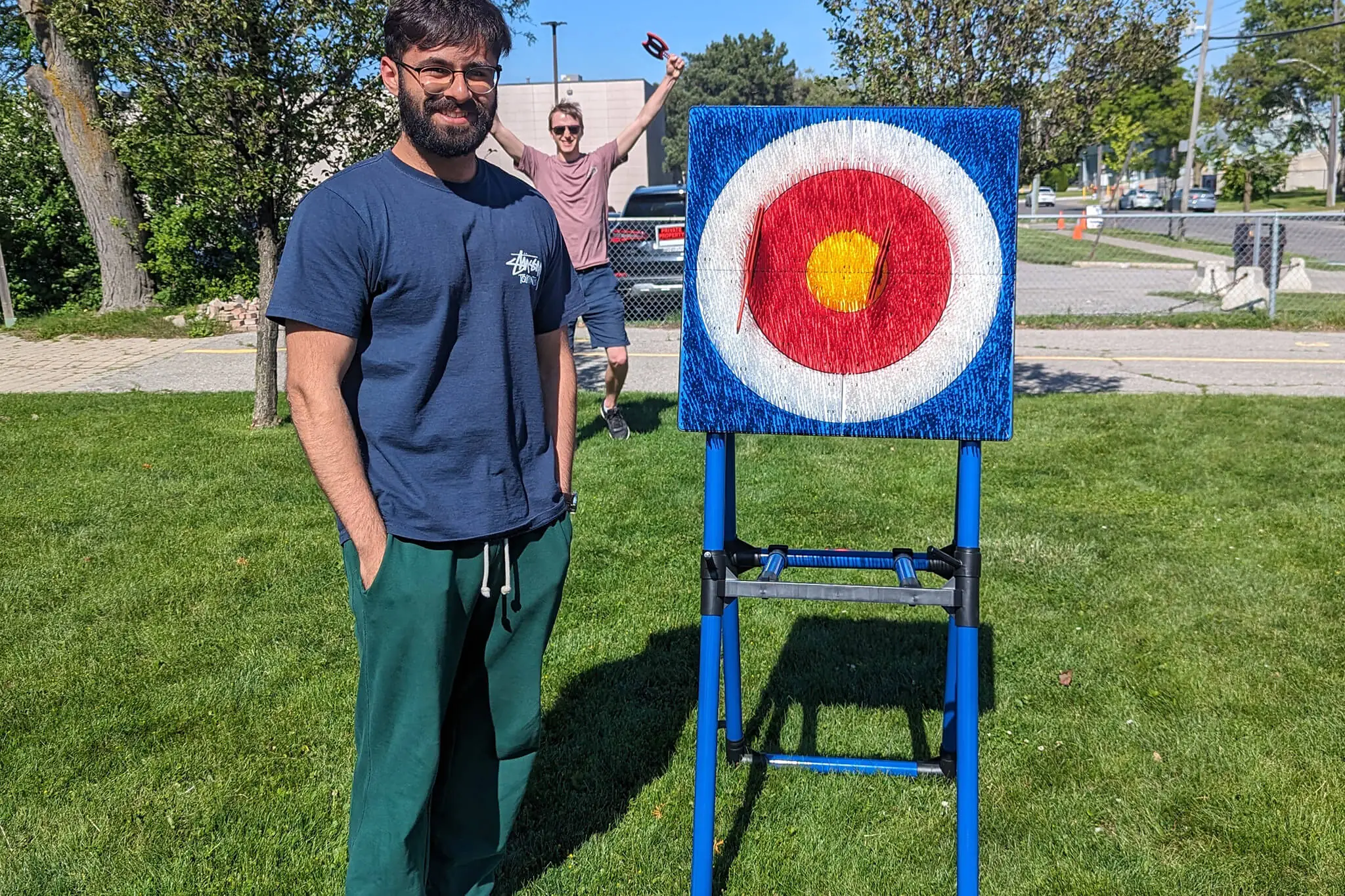  A man stands beside a target on a lawn, representing teamwork and focus among YuJa's team members.