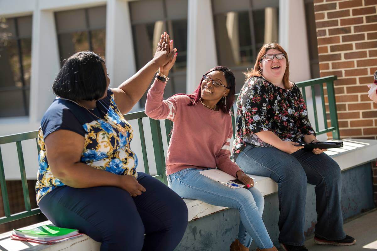 Three women sitting on a bench, one woman giving a high five.