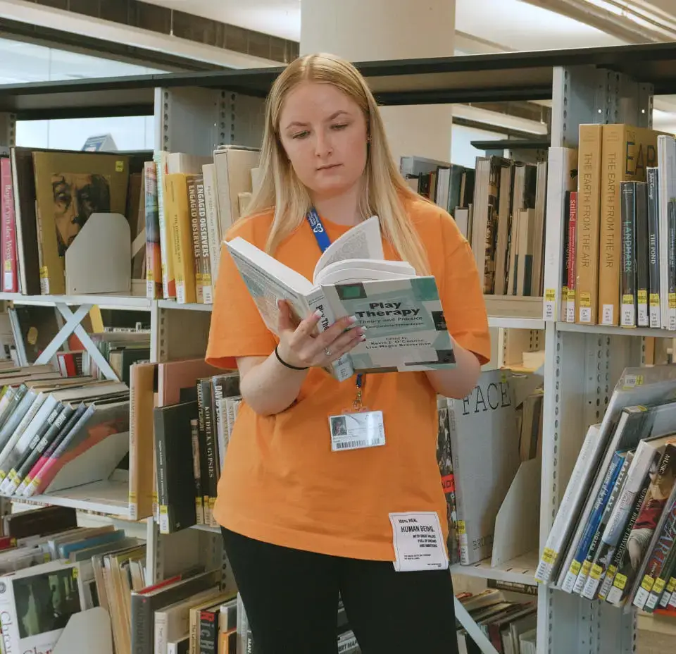 A woman in an orange shirt reading a book at Canterbury Christ Church University.