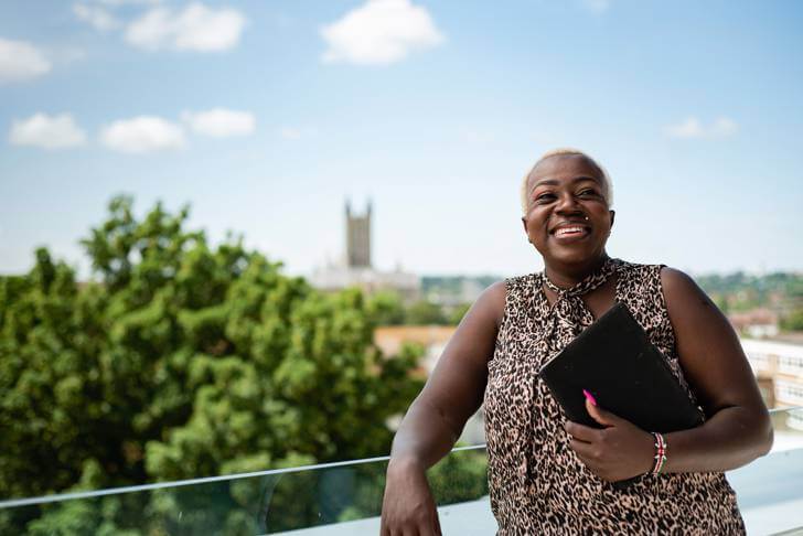 A woman on a balcony at Canterbury Christ Church University, using a laptop to work.