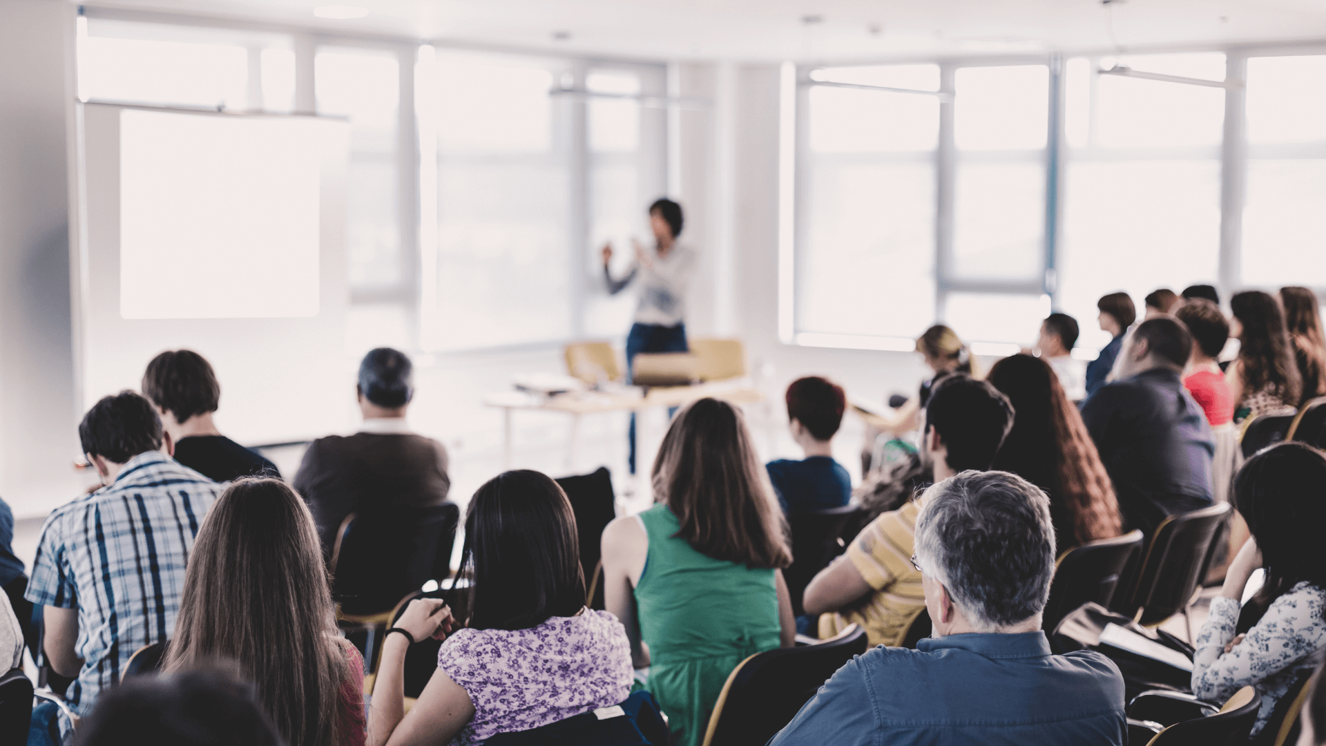 A group of people are facing a speaker in the front of a training room.