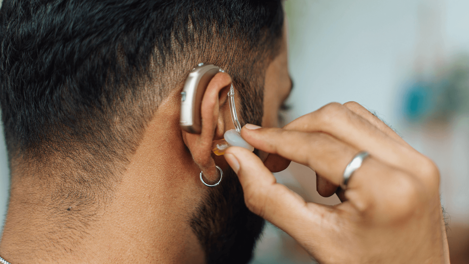 A bearded man wearing a deaf device to enhance his hearing.