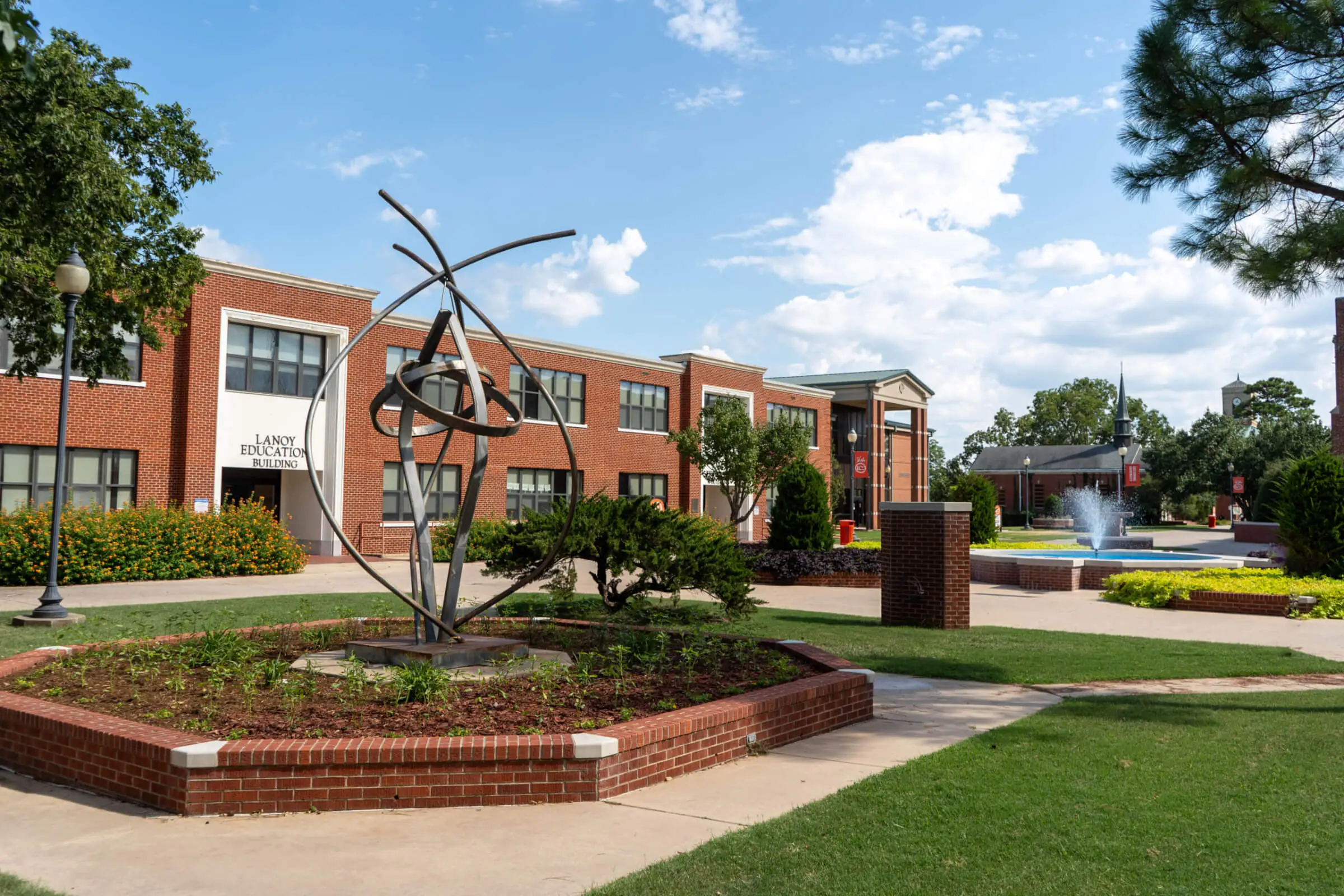 East Central University buildings and the courtyard with a sculpture and fountain in the foreground.
