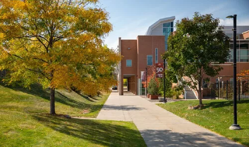 A walkway leading to Red Rocks Community College building surrounded by trees and grass.