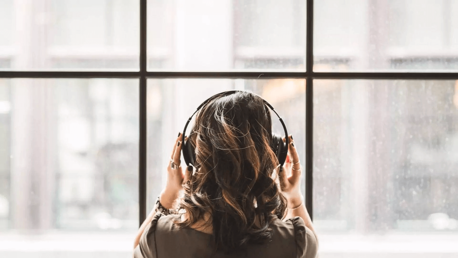 A woman wearing headphones looks out a window.