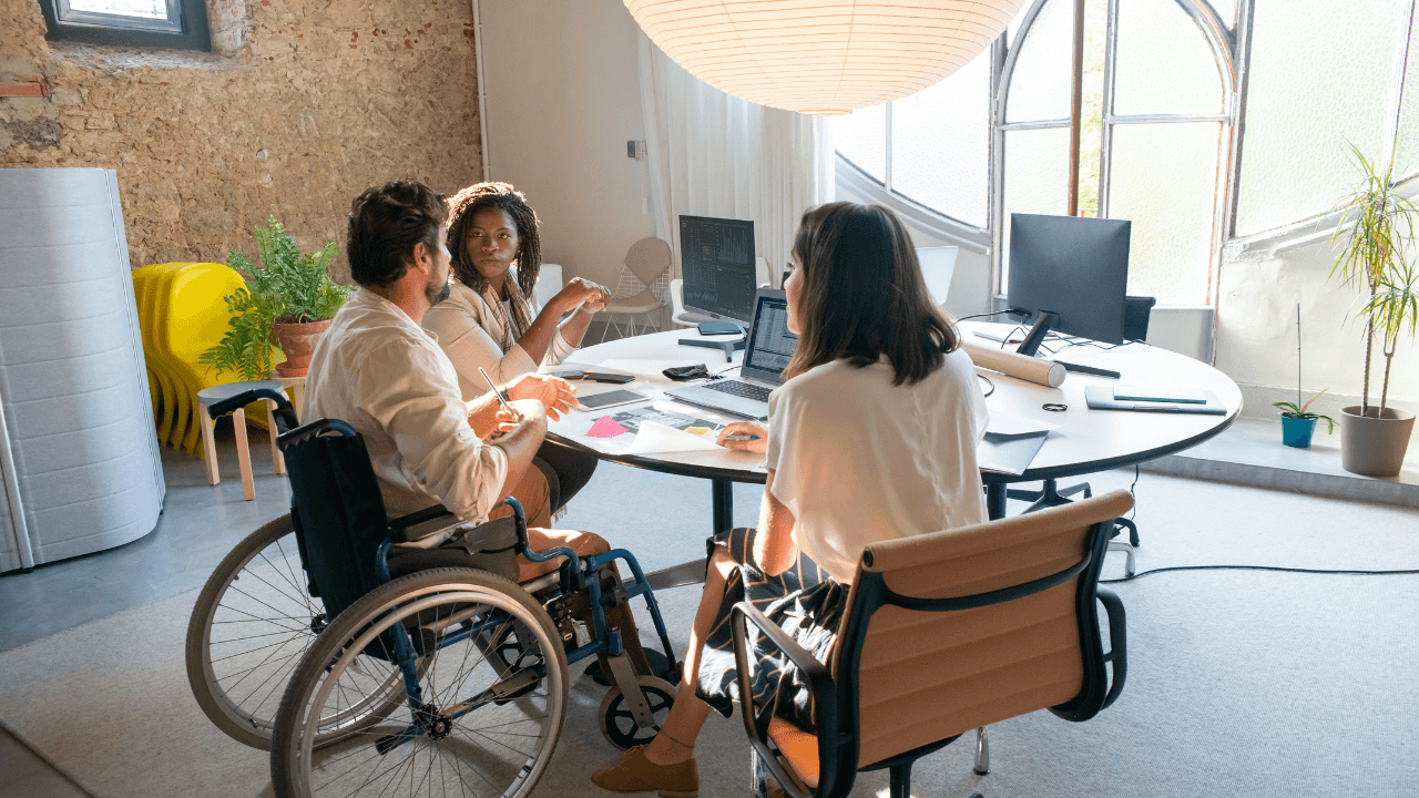 Two ladies and a man at a table discussing a project.