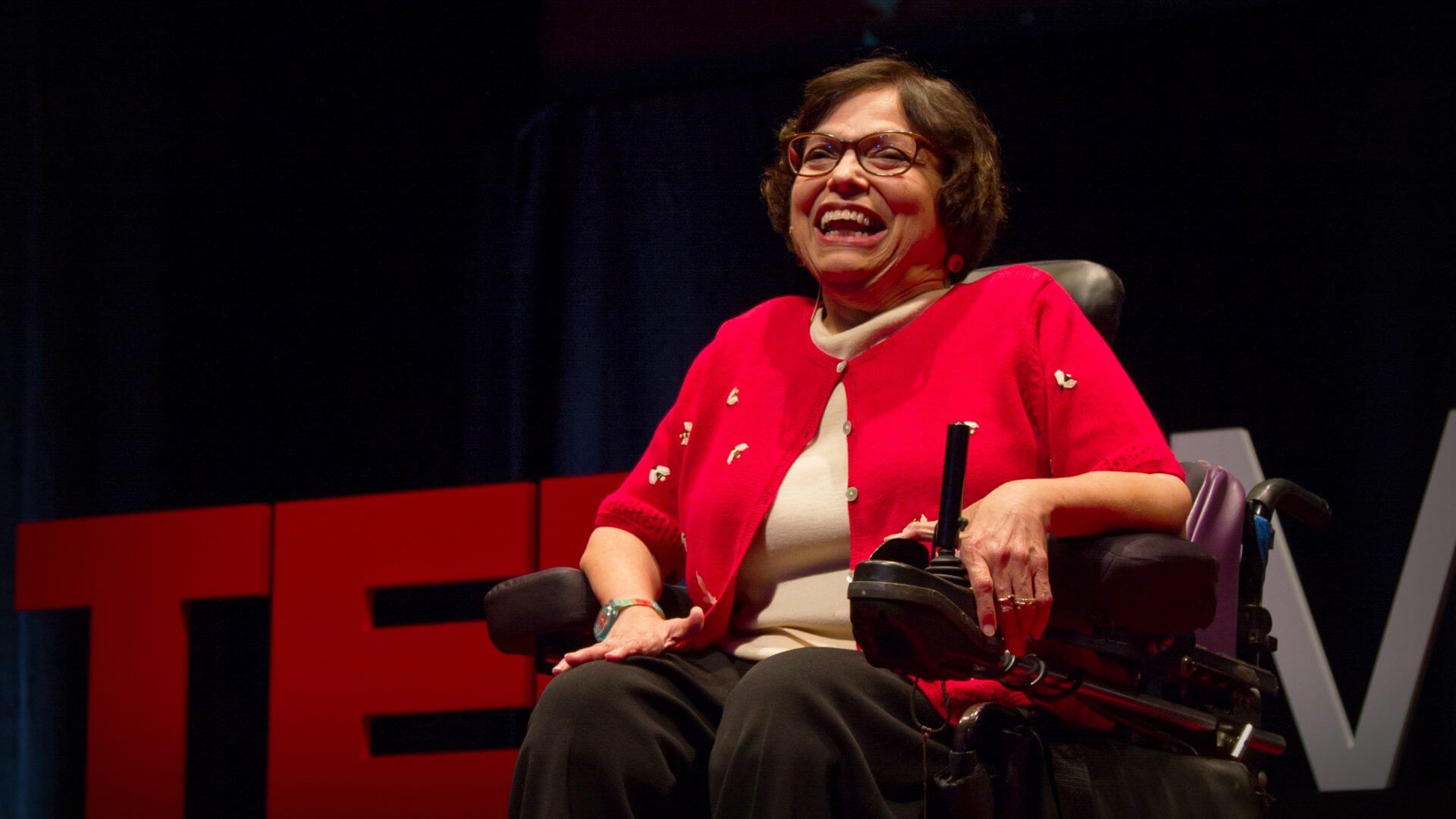 Judy Heumann at her TED Talk with the TED sign behind her.