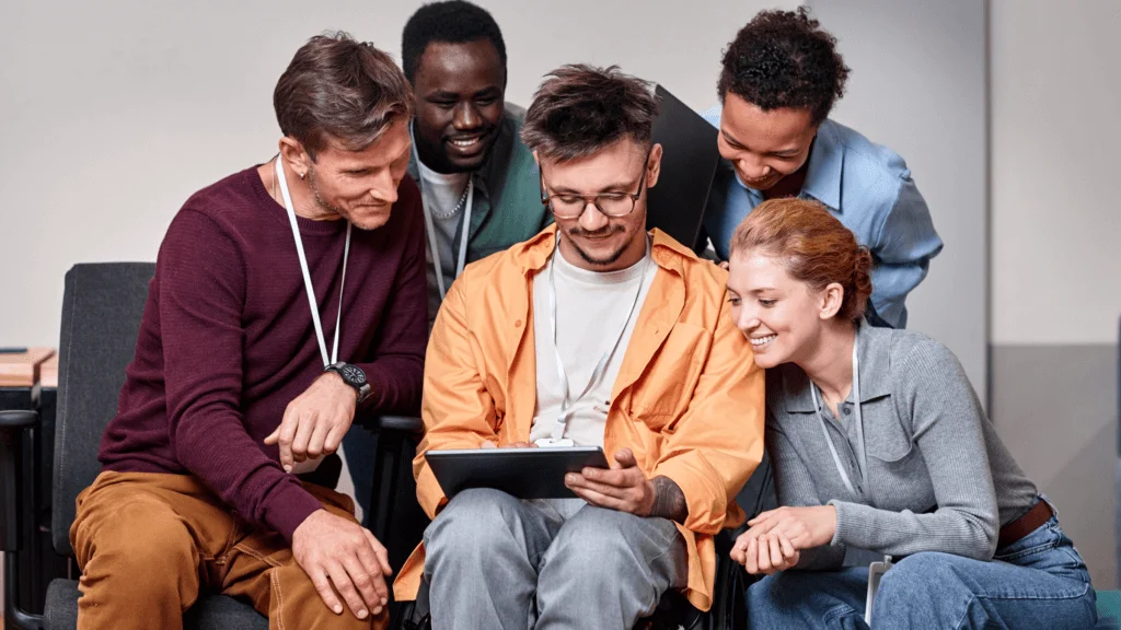 People working as a team, huddled around a young man holding a tablet.
