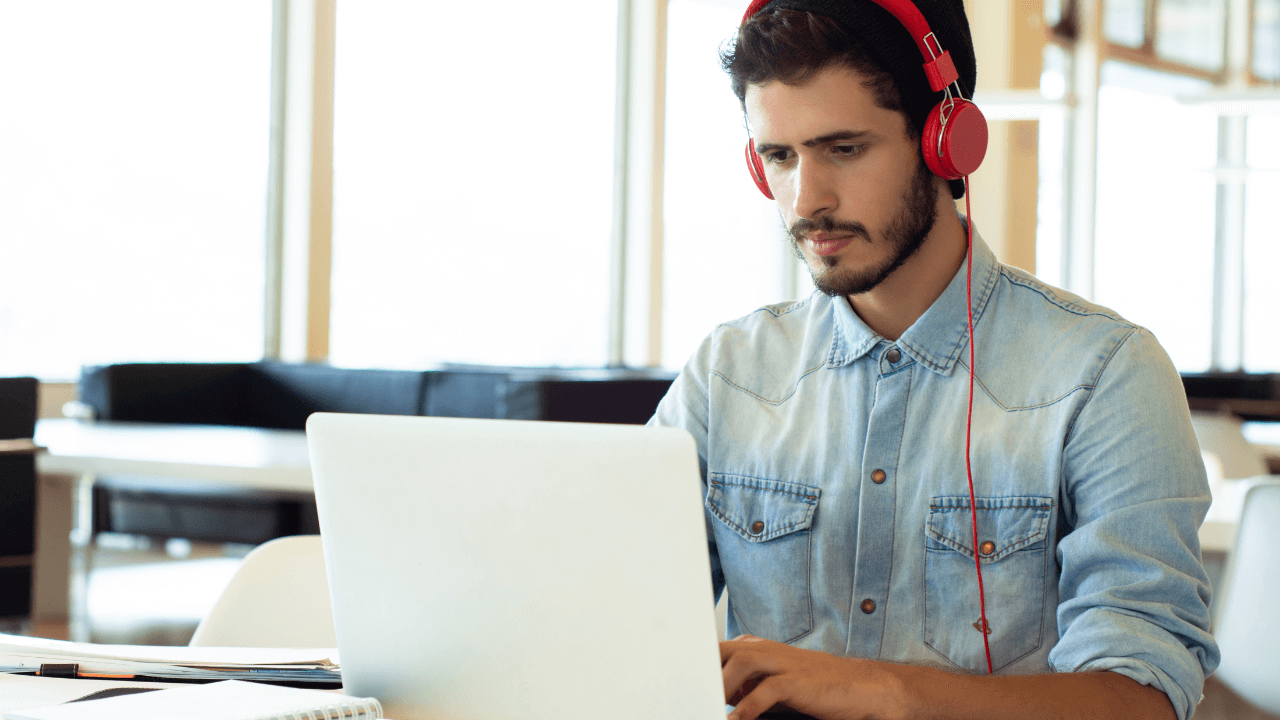 A young man wearing headphones looks at a computer.