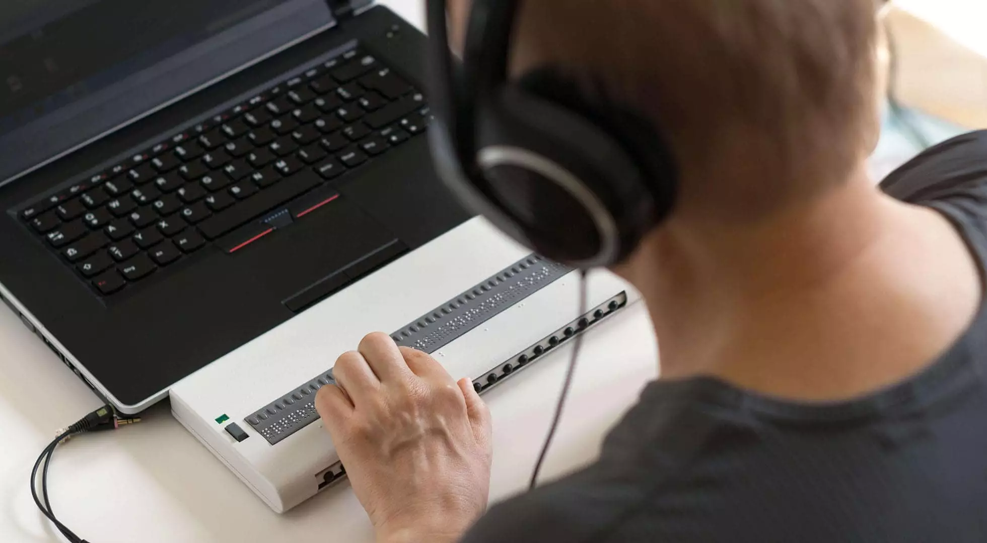 Person wearing headphones using a screen reader with braille output.