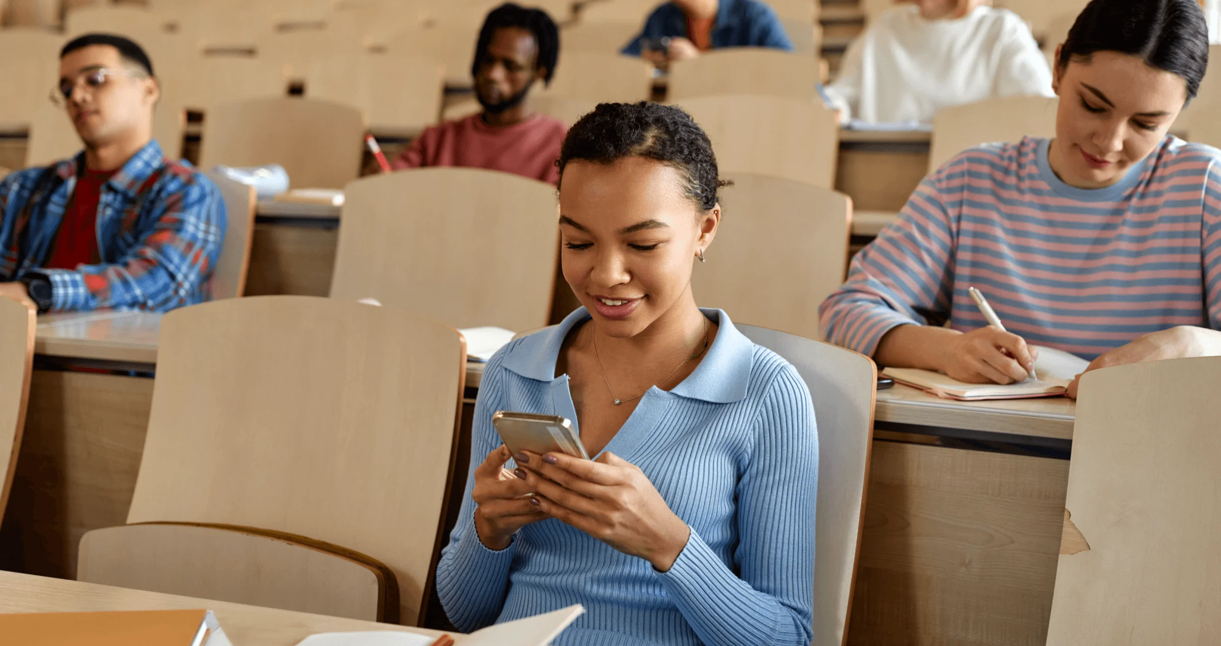 A young woman sitting in a lecture hall and using the YuJa Engage app, surrounded by other students.