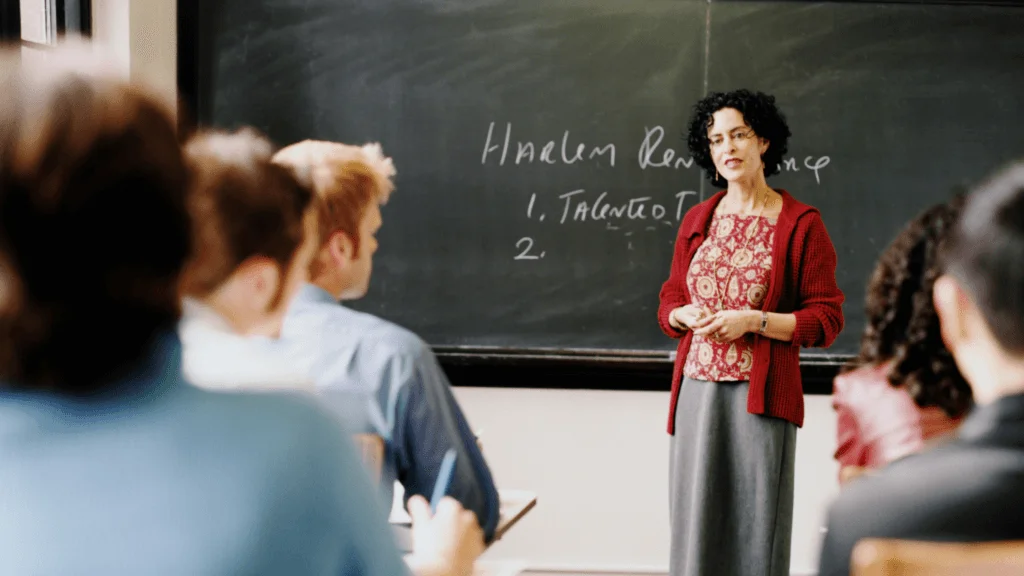 Teacher stands at blackboard with students in the foreground.