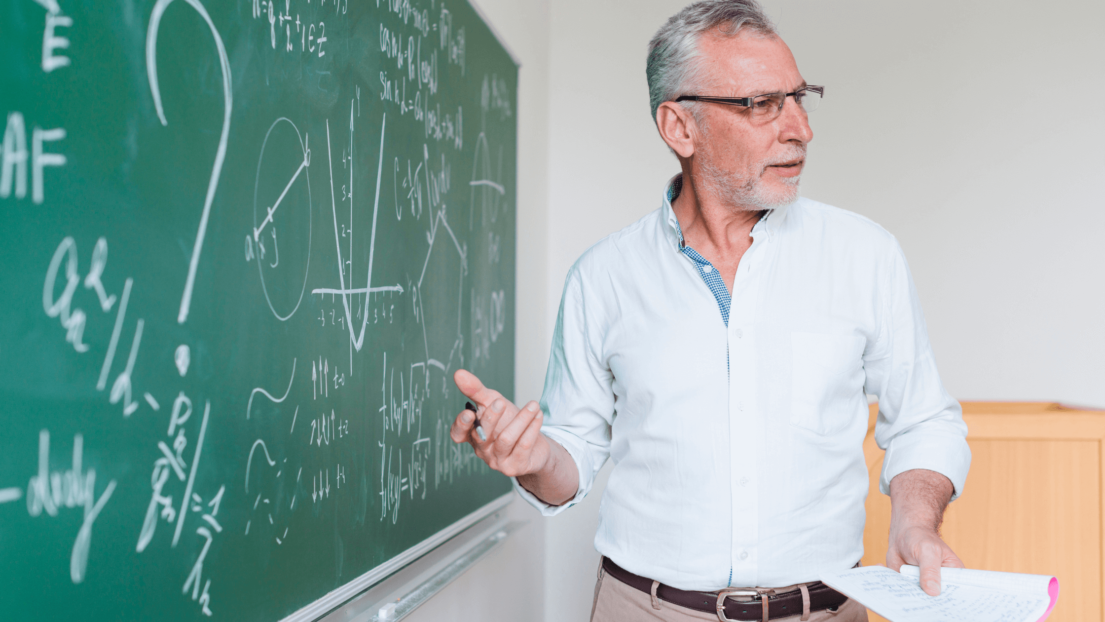 Teacher in front of blackboard with mathematical formulas written on it.