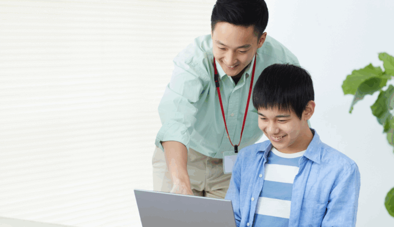 A teacher works closely with a student on his laptop.