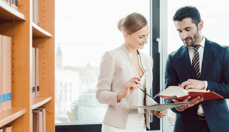 Two lawyers are having a discussion and reading from a large law book.