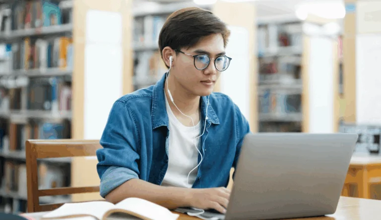 A student with glasses is looking at a laptop.