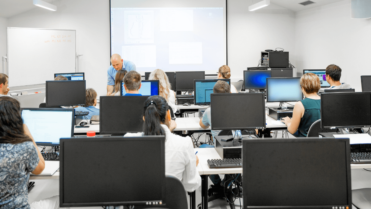A college professor helping students with exams in a computer testing center.