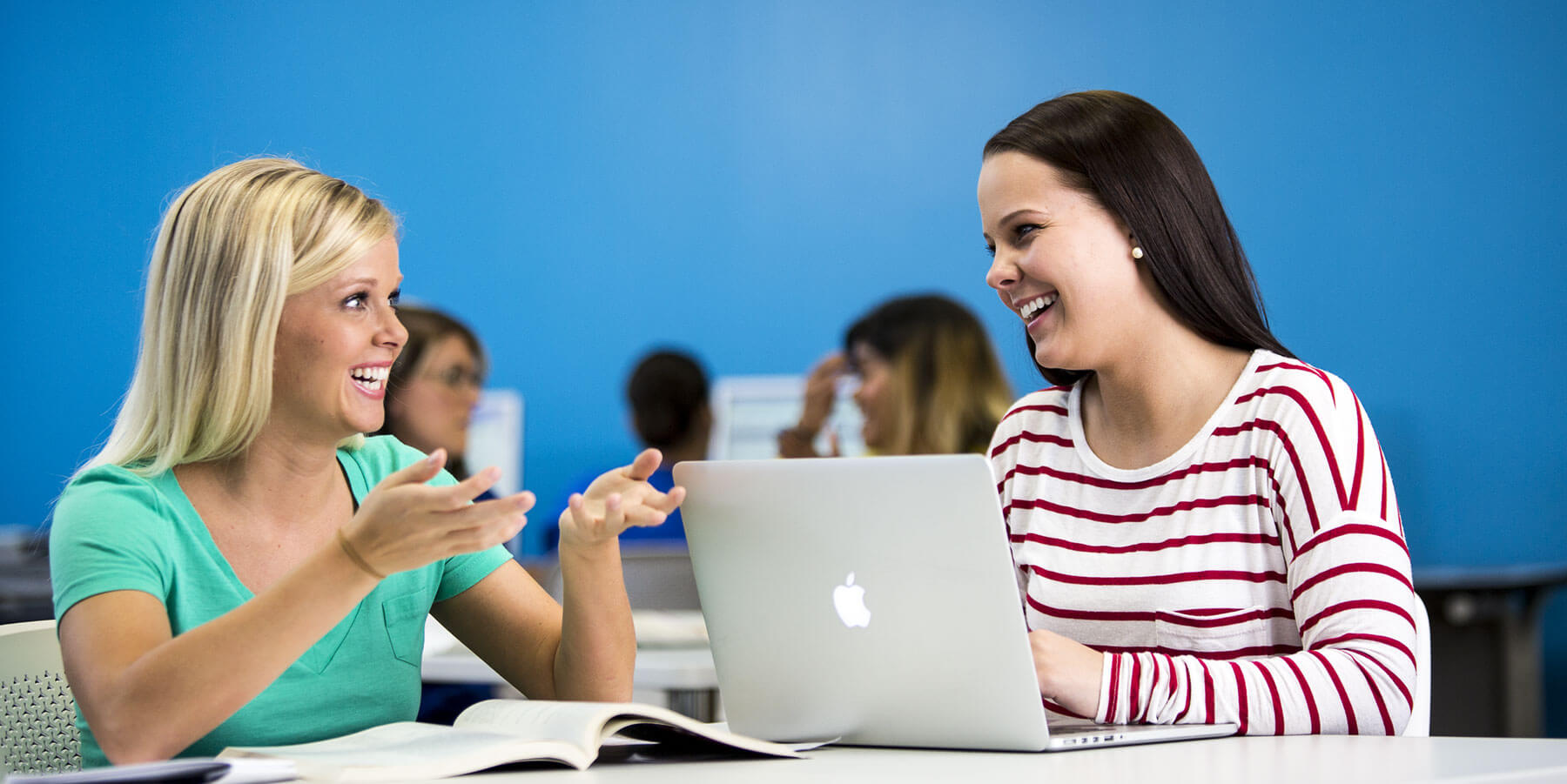 Two women sitting at a table, engrossed in their work on a laptop.