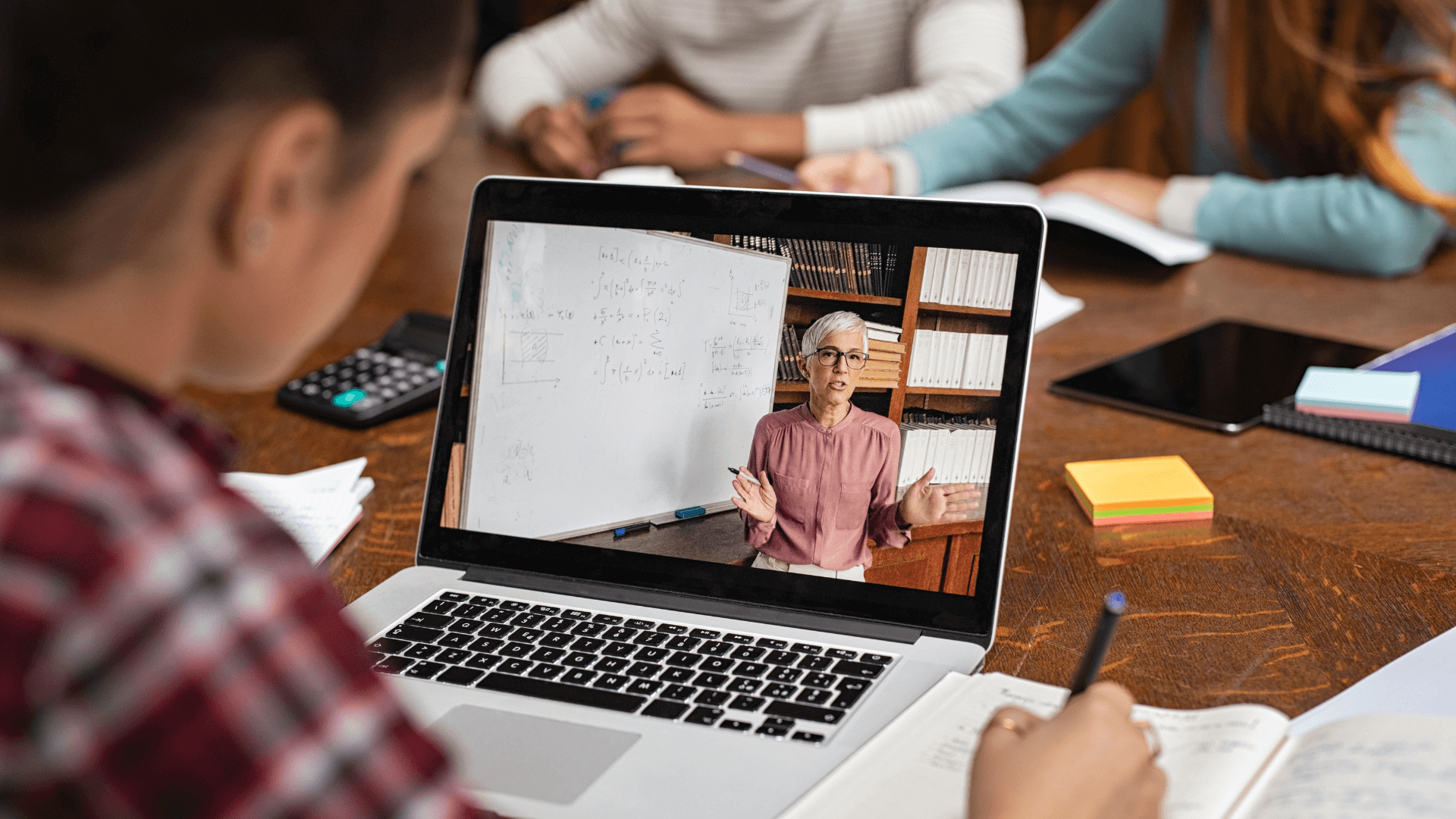 A student looks at a laptop showing an instructor explaining something using a whiteboard.