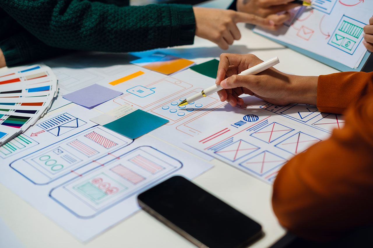 two UX designers discussing mobile low fidelity wireframe prototypes on paper