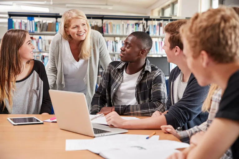 female teacher working with four university students in the library