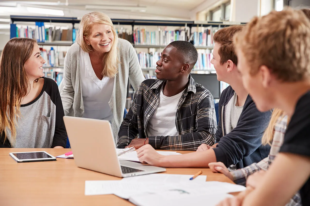 female teacher working with four university students in the library
