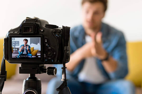 A man with a video camera in front of a couch.