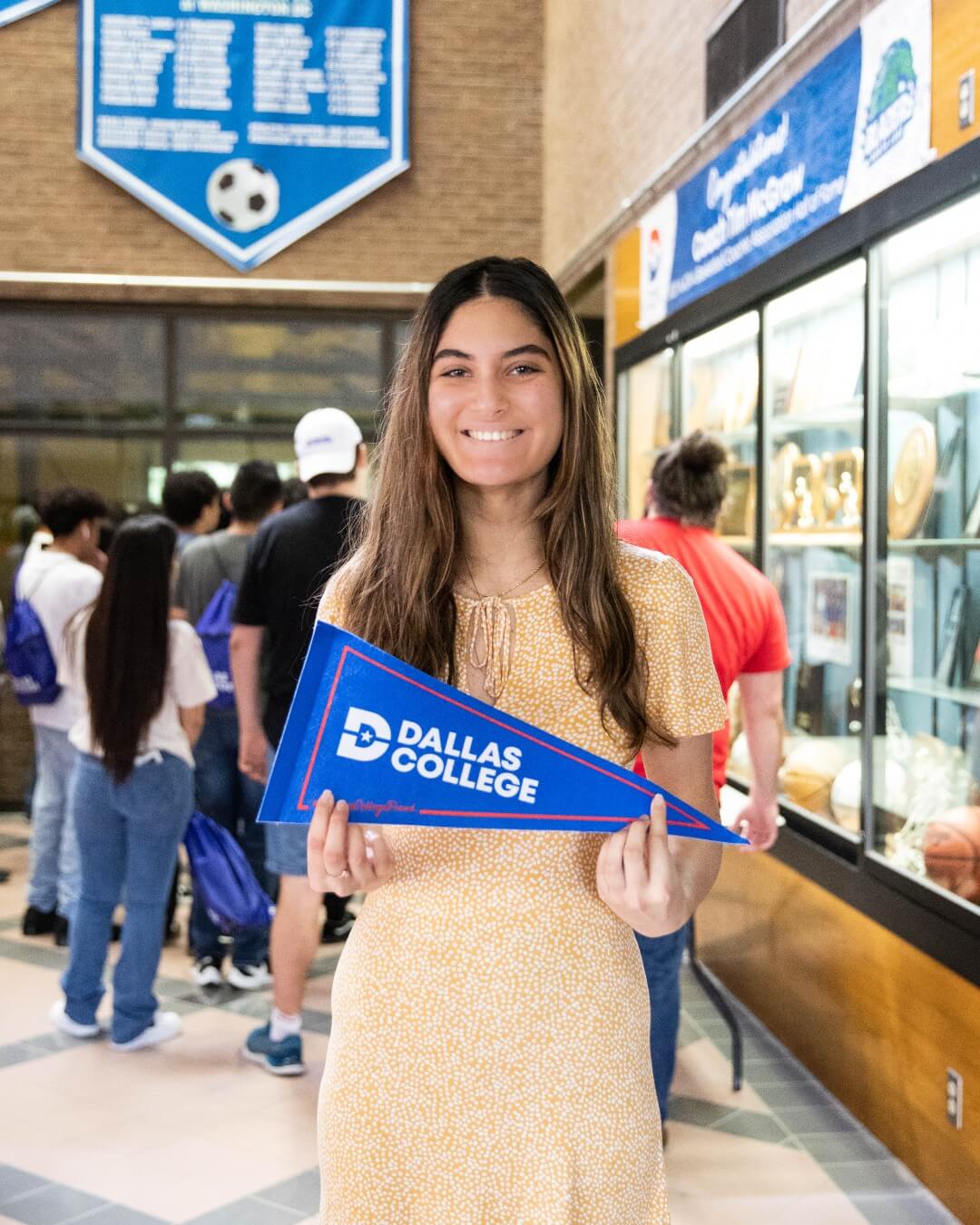 A girl proudly holds a blue and white pennant with Dallas College logo.