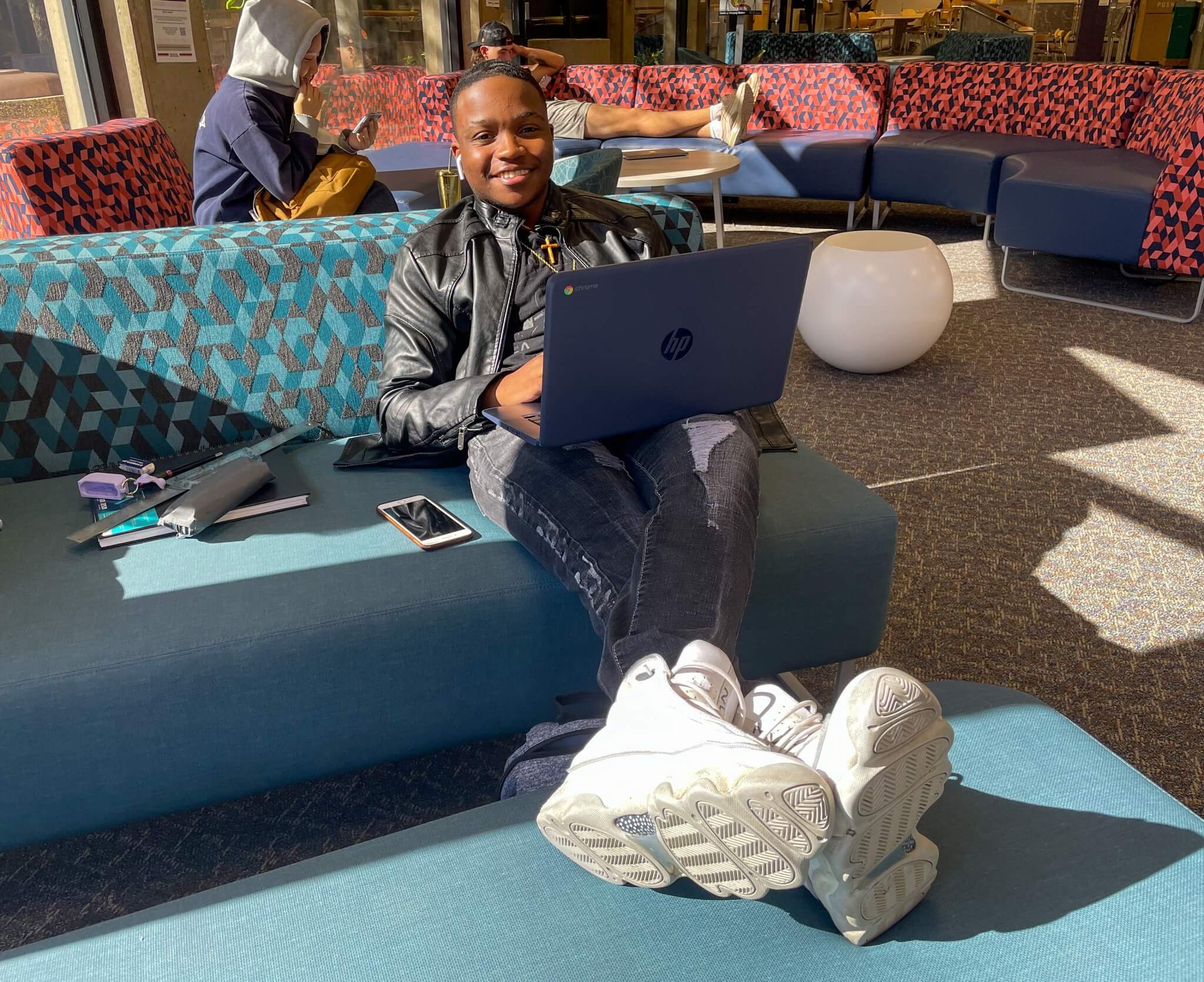 A young man sitting on a couch with his laptop at Dallas College. 