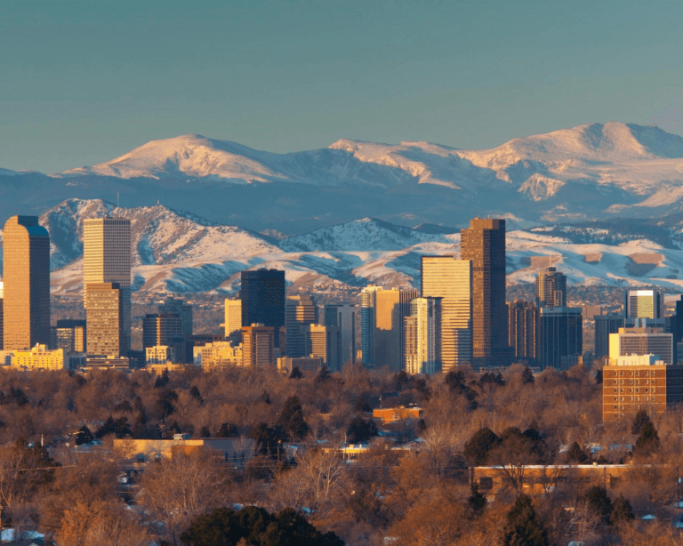 Denver city skyline with tall buildings and mountains in the background.