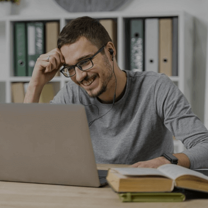 A man in glasses working at a desk with a laptop and books.