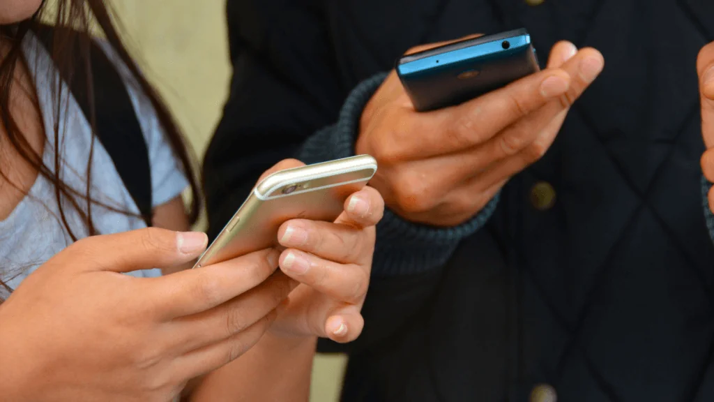 A close up image of mobile phones in people's hands.