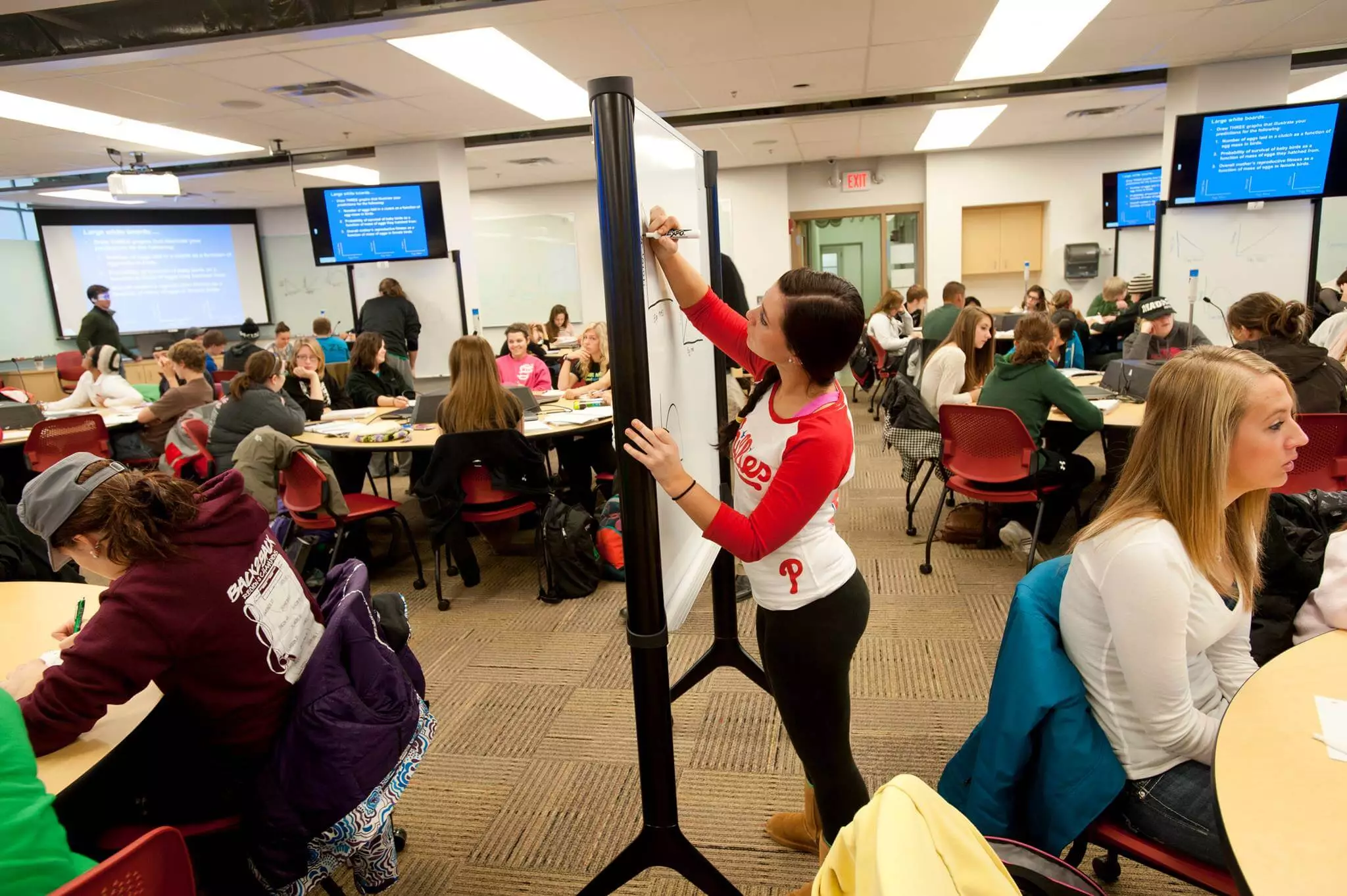 A diverse group of students sitting in a classroom with a white board in the background.