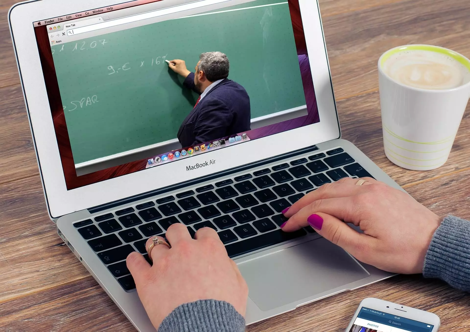 A person sitting at a desk using a laptop with a chalkboard on it.