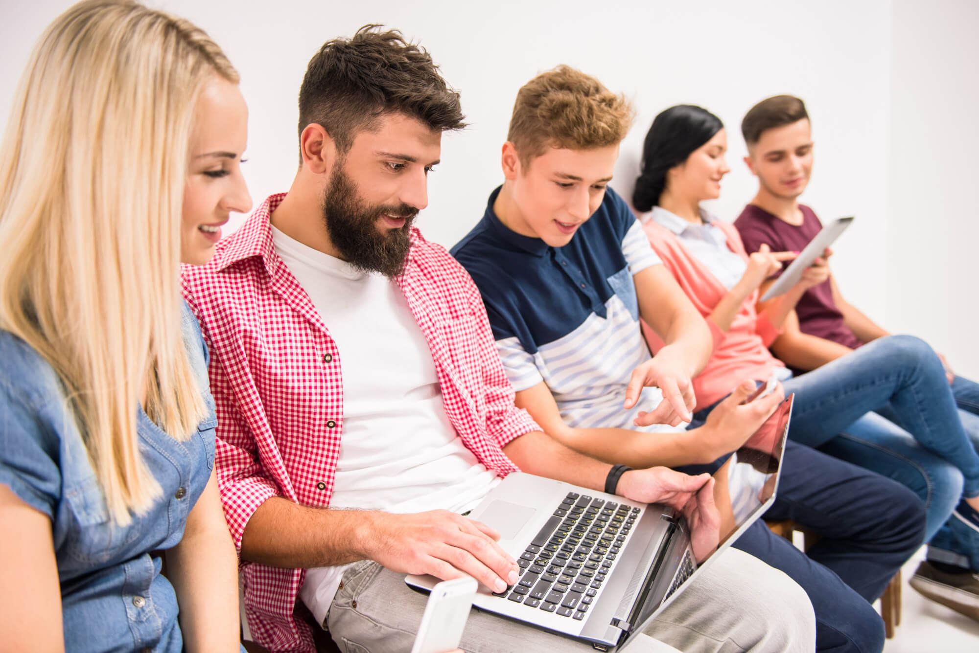 A diverse group of individuals sitting on a bench, engrossed in their laptops.