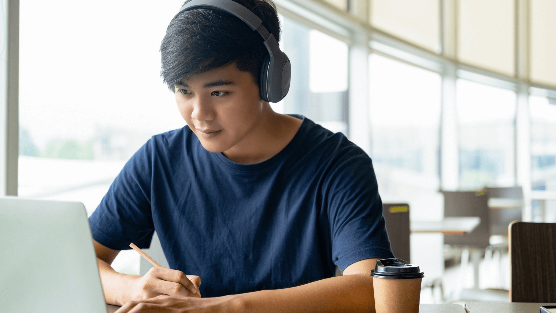 A focused young man wearing headphones sits at a table.