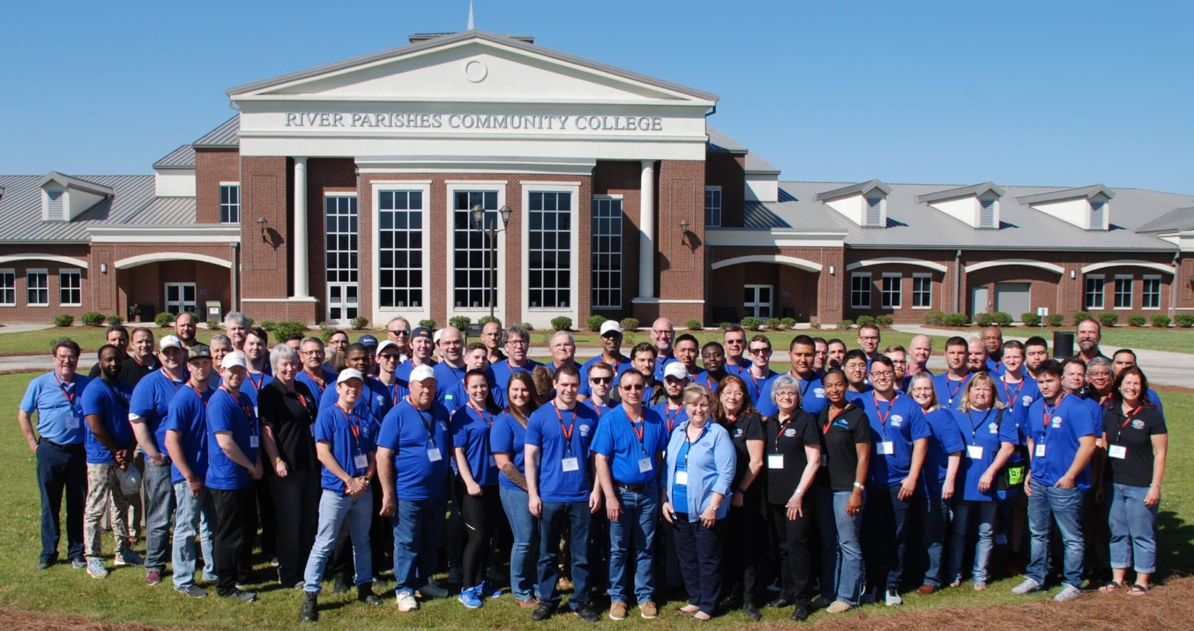 Employees wearing blue shirts pose outside River Parishes Community College.