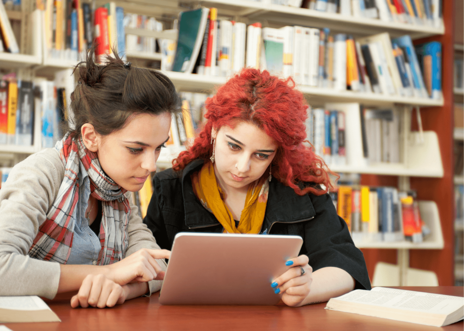 Two students look at tablet in a library.