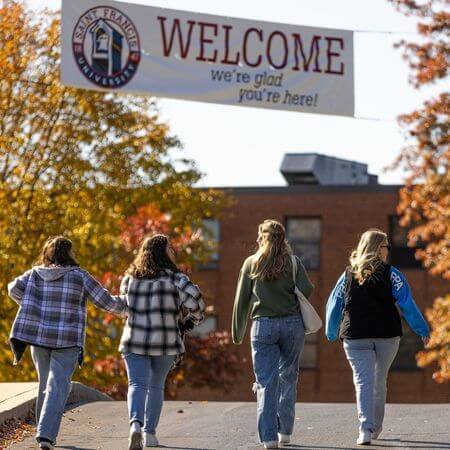 four students walking up to a welcome banner at Saint Francis University.