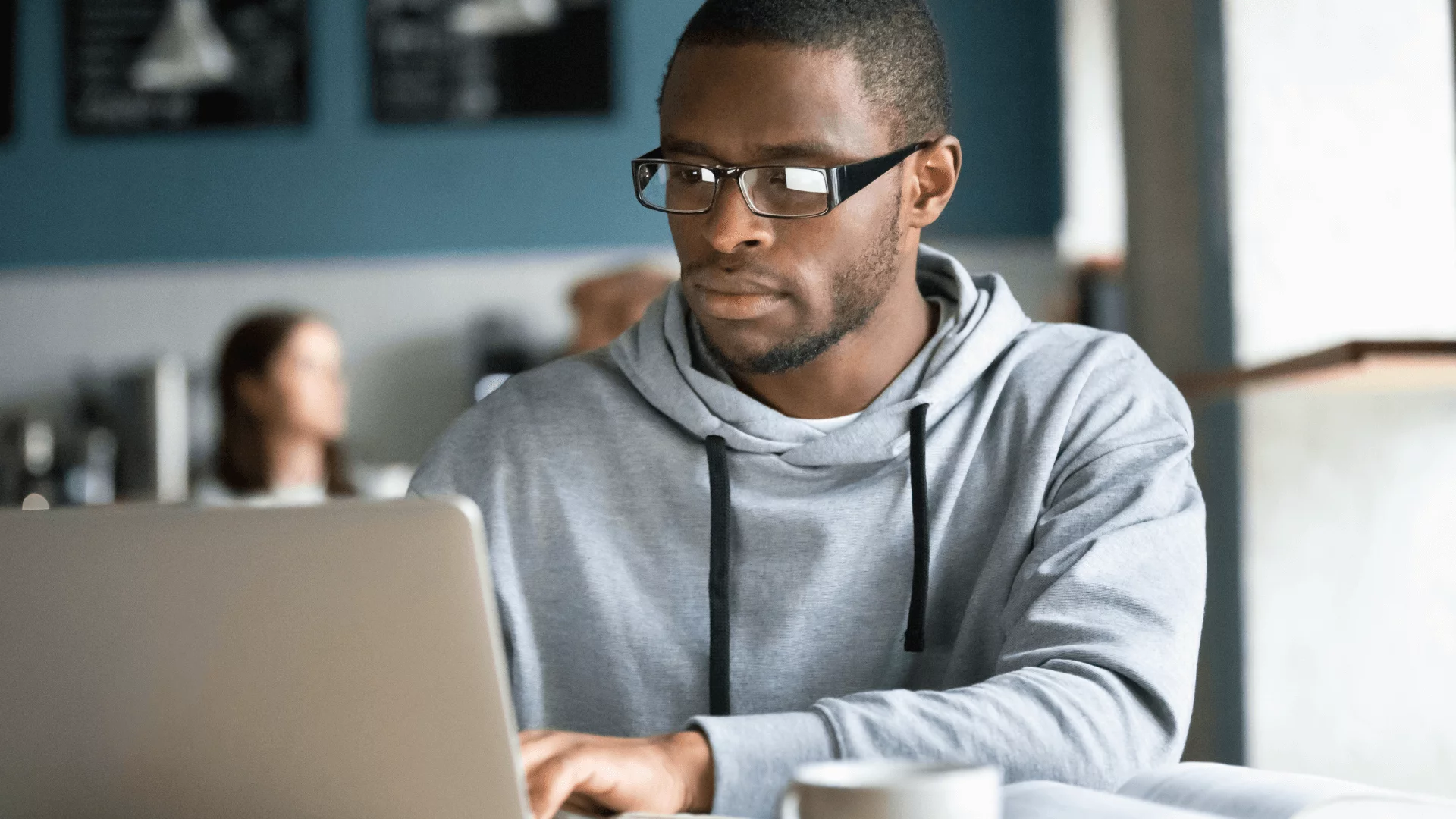 A man in glasses is using a laptop in a coffee shop.