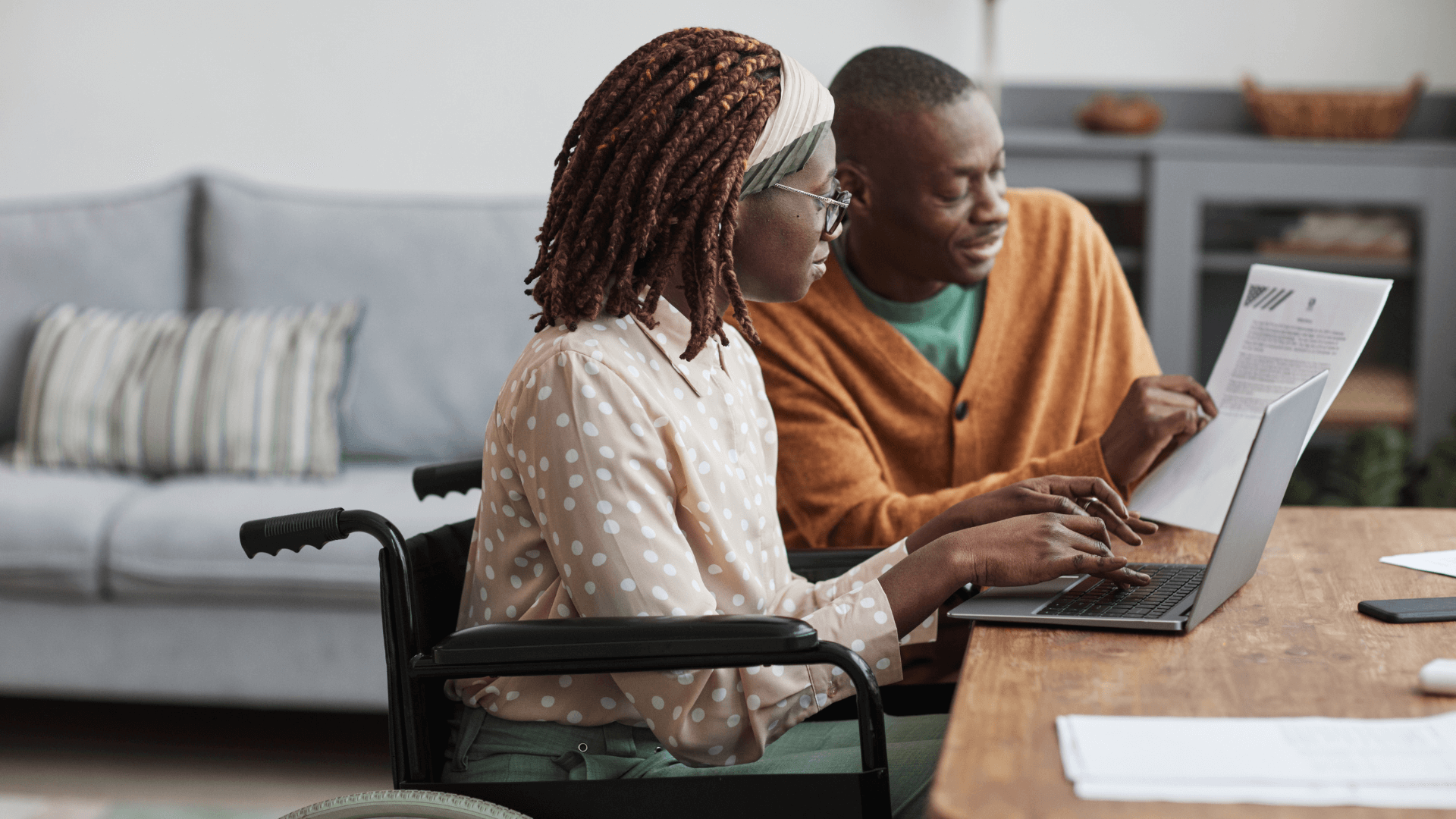 A man and woman in wheelchairs sitting at a table with a laptop.