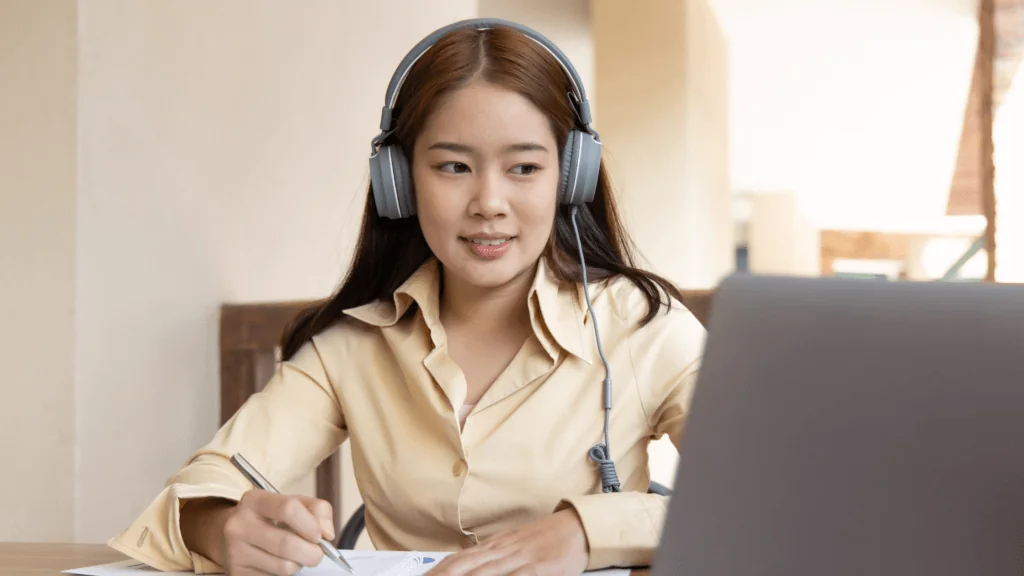 Woman wearing headphones looks at laptop.