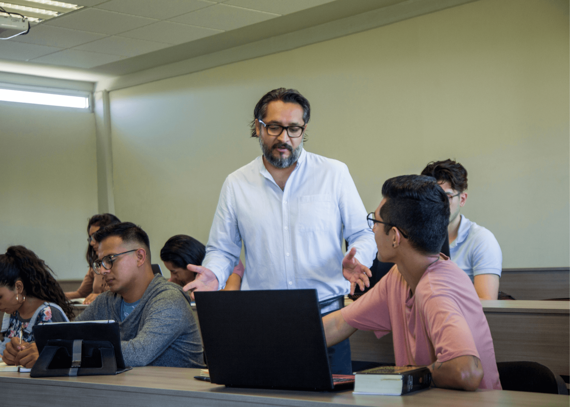 Male teacher talks to college-aged student who is using a computer.