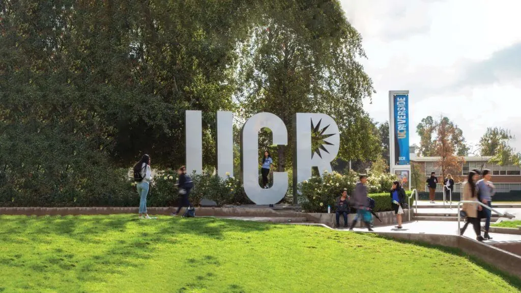 A group of people walking in front of UC Riverside sign.