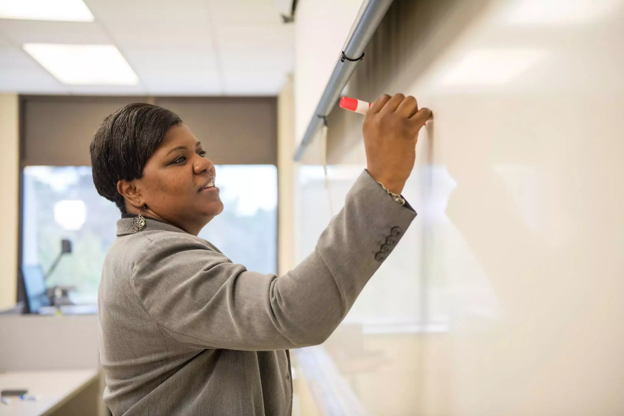 A professional woman in a business suit writing on a whiteboard.