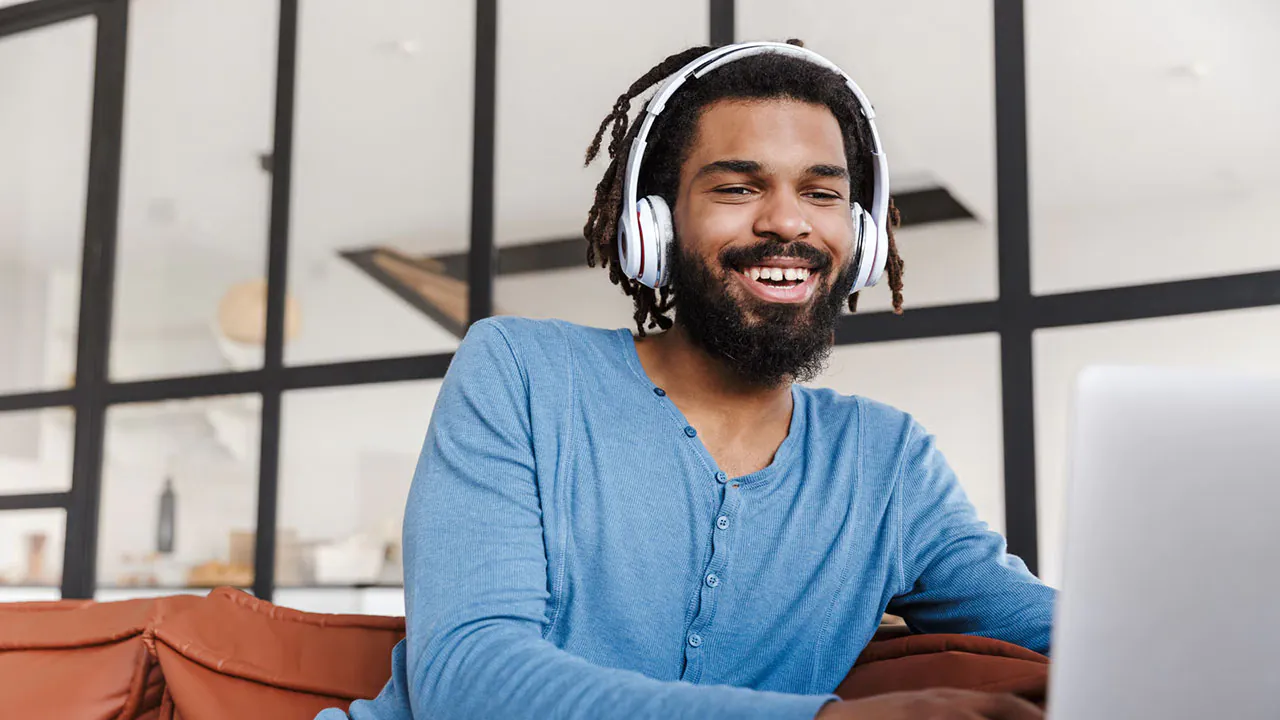 Man in a blue shirt sitting on a couch listening to a video with white headphones